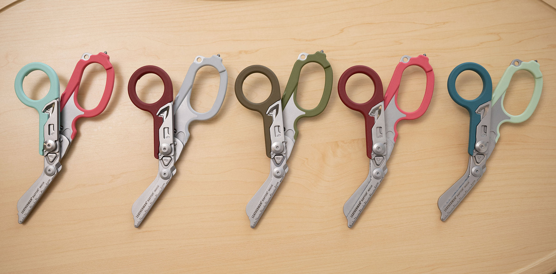 Five pairs of colorful Leatherman Raptor Rescue shears displayed on a table, highlighting their unique design and colors.