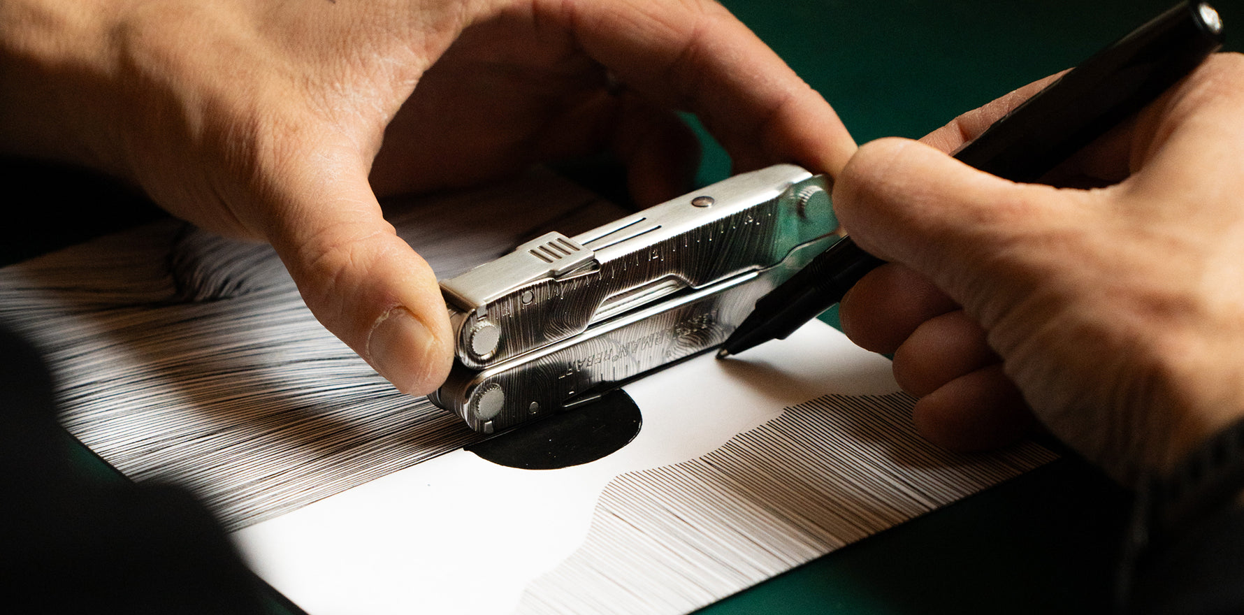 Person using the ruler on a stainless steel Leatherman Rebar to draw lines on a piece of paper.