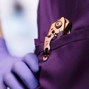 Translation missing: en.Rose Gold Raptor® Rescue tool clipped to a purple scrub pocket held by a gloved hand
