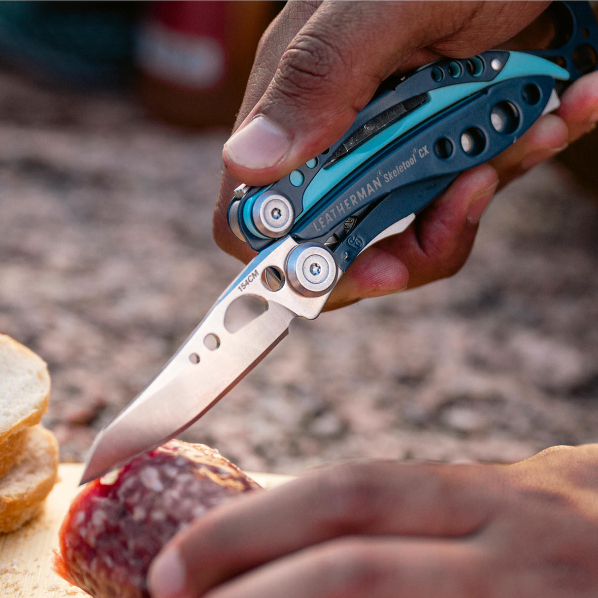 Translation missing: en.Hand using a Nightshade Leatherman Skeletool CX knife to slice cured meat on a cutting board