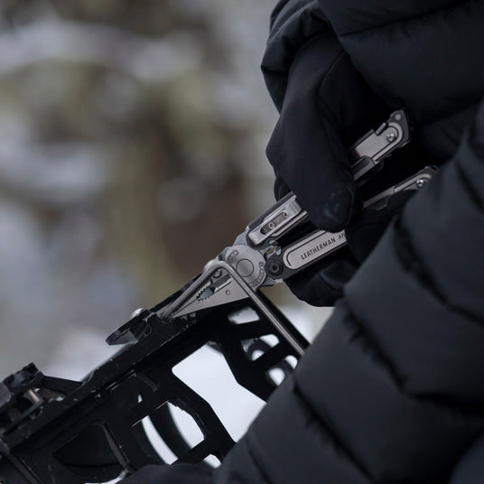 Someone using the pliers on a Leatherman ARC to fix a binding on a snowboard.