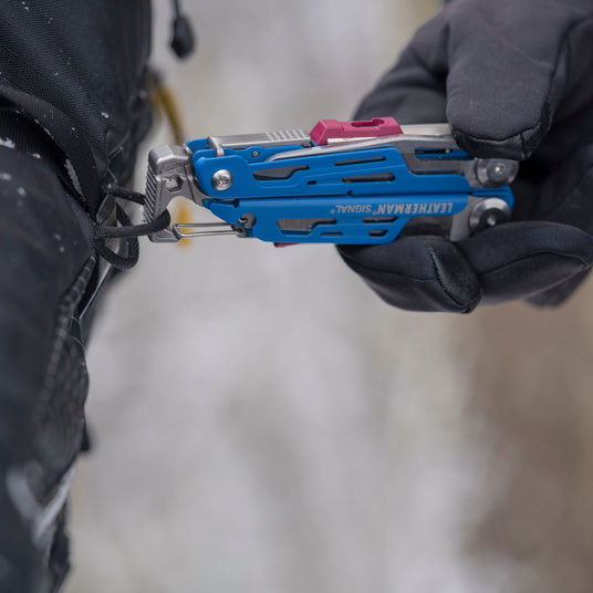 Someone holding a Leatherman Signal that is attached to a backpack.