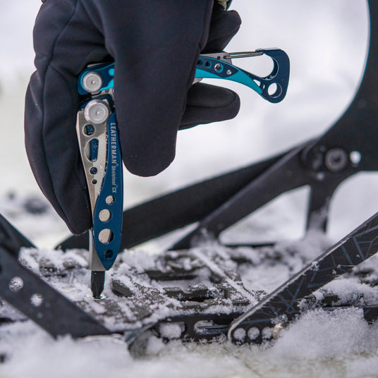 Someone using a Skeletool CX to tighten the binding on a snowboard.